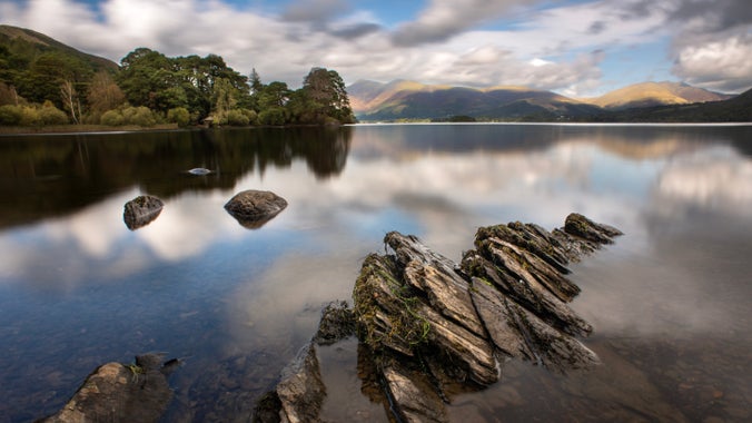View across a still lake towards mountains and woodlands